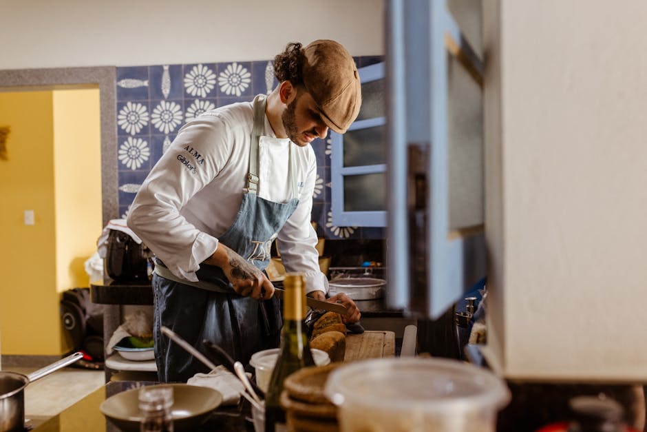 Chef wearing uniform and cap slicing bread in a contemporary kitchen setting.
