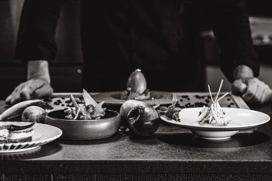 Chef arranges gourmet dishes on a table in a black and white setting.
