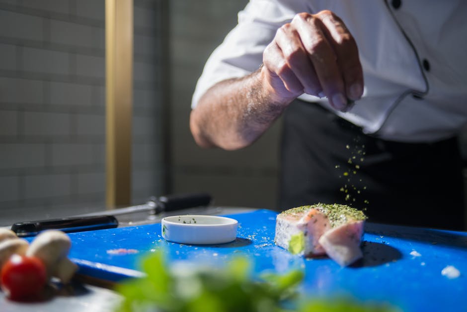 A chef skillfully seasons a gourmet dish in a modern kitchen, highlighting culinary expertise.