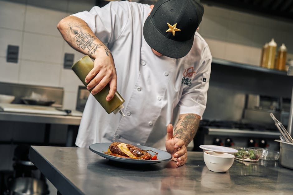 Chef garnishing a gourmet dish with sauce in a professional kitchen setting.